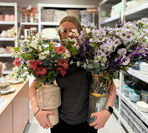 Medarbejder fra Basic & More der holder vaser frem med kunstige blomster i